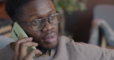 Cep telefonuyla konuşan neşeli Afro-Amerikalı adamın yakın çekimi evde sohbete odaklandı. İnsanlar ve cep telefonu bağlantısı kavramı.