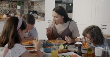 Mutlu aile, anne, baba, oğul ve kız, öğle yemeği yiyorlar, lezzetli yemekler yiyorlar, modern evdeki mutfağın tadını çıkarıyorlar. İnsanlar ve yaşam tarzı kavramı.