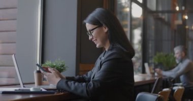 Akıllı telefon kullanan mutlu bir bayan girişimci. Sonra laptopla kafedeki iş iletişimine odaklanmış. Modern teknoloji ve iş kadını kavramı.