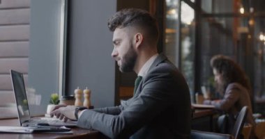 Laptop kullanan heyecanlı genç iş adamı kafeterya masasında oturmuş başarılı bir iş projesinin keyfini çıkartıyor. Pozitif duygu ve girişimci konsepti.