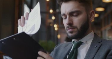 Takım elbiseli ciddi bir genç iş belgesi okuyor. Yazıyor. Kafede mali bilgileri kontrol ediyor. Girişimci ve başarılı başlangıç konsepti.