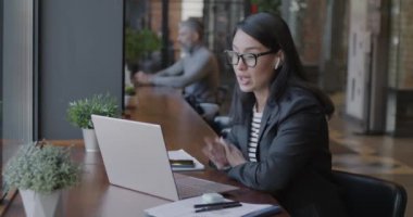 Neşeli genç iş kadını, kafedeki masada dizüstü bilgisayar ve kablosuz kulaklıkla online video görüşmesi yapıyor. Modern iletişim teknolojisi ve iş konsepti.