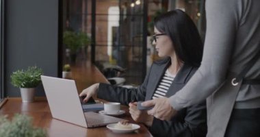 Başarılı bir iş kadını, akıllı telefon ve garsonla konuşan NFC ödeme makinesiyle kafede sipariş veriyor. Modern teknoloji ve iş adamı kavramı.