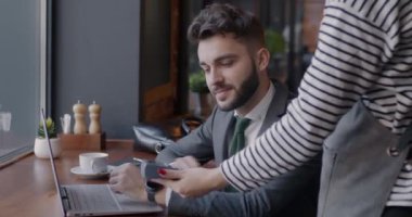 Neşeli genç işadamı, elinde ödeme makinesi olan garsonun kredi kartıyla kafede ödeme yapıyor. Modern yaşam tarzı ve iş konsepti.