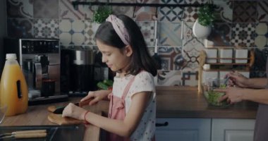 Yavaş çekimde salata pişiren mutlu küçük kızın portresi sağlıklı sebze yemeği hazırlıyor sonra kameraya bakıyor ve mutfakta gülümsüyor. Çocukluk ve yaşam tarzı kavramı.