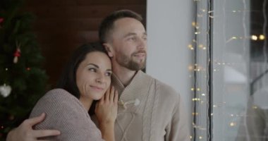 Sevgili çift, kucaklaşıp pencereden dışarı bakıyor ve evde Noel kutlamasıyla eğleniyor. Romantik ilişki ve özel olay kavramı.
