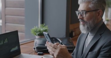 Kendine güvenen olgun iş adamı kafedeki aleti kullanarak akıllı telefondan ekrana dokunuyor. İş iletişimi ve modern cihaz kavramı.