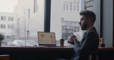 Hırslı iş adamı cep telefonuyla konuşuyor. Laptop kullanarak ve kafede kağıt okuyarak iş hakkında konuşuyor. İş ve profesyonel iletişim kavramı.