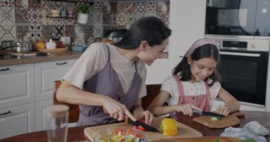 Genç bir kadın ve sevimli bir çocuk sebze salatası hazırlıyor öğle yemeği pişiriyor ve evdeki mutfak masasında konuşuyor. Halk ve aile yaşam tarzı kavramı.