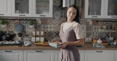 Öğle yemeği için sofra kuran genç ve güzel bir kadının ağır çekimde tabakları gülümseterek eve girmesi. Ev hayatı ve beslenme konsepti.