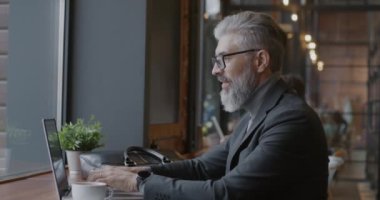 Keyifli, olgun iş adamının portresi laptoptan iyi haberler alıyor ve profesyonel başarının tadını çıkarıyor. İş başarısı ve modern teknoloji kavramı.