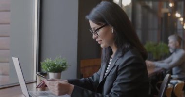 Neşeli iş kadını, kafenin içinde kredi kartı ve dizüstü bilgisayar kullanarak online ödeme yapıyor. Modern bankacılık teknolojisi ve iş konsepti.