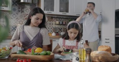 Genç bir kadın yardımcı kızıyla yemek pişirirken bir adam cep telefonuyla konuşuyor ve mutfakta meyve suyu içiyor. Modern yaşam tarzı ve mutlu aile kavramı.