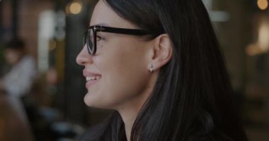 Kameraya dönüp kafenin içinde gülümseyen neşeli genç iş kadınının yavaş çekim portresi. Hırslı kişi ve olumlu duygu konsepti.