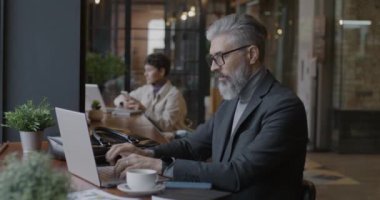 Yetişkin bir iş adamı dizüstü bilgisayarla yazarak çalışıyor sonra da cep telefonuyla kafede iş hakkında konuşuyor. Modern teknoloji ve iş geliştirme kavramı.
