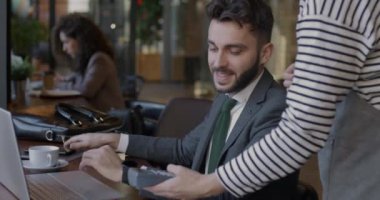 Akıllı telefon ve NFC makinesiyle kablosuz ödeme yapan kendine güvenen genç işadamı kafede garsonla konuşuyor. Modern cihaz ve iş konsepti.