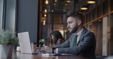 Bir grup insanla birlikte kafede oturan genç iş adamının bilgisayar daktiloyla yazma çalışmasının yan görüntüsü. İş adamı ve modern yaşam tarzı konsepti.