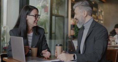 Neşeli iş adamları, ellerinde kahve fincanlarıyla dizüstü bilgisayara bakıp gülerek konuşuyor. İş birliği ve olumlu duygu kavramı.