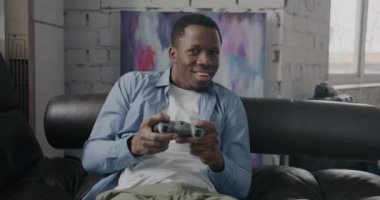 Heyecanlı Afro-Amerikalı birinin portresi oyun oynarken joystickle kazanmak dairedeki kanepede eğlenmek. Eğlence ve oyun konsepti.