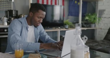 Genç Afrikalı Amerikalı serbest yazar dizüstü bilgisayarla evde mutfakta çalışıyor. Serbest meslek ve modern teknoloji konsepti.
