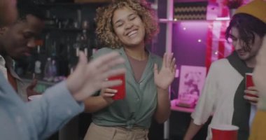 Akşamki partide kadehleri içkilerle tokuşturup müzik eşliğinde dans eden mutlu gençlerin ağır çekimleri. Modern yaşam tarzı ve içecek konsepti.