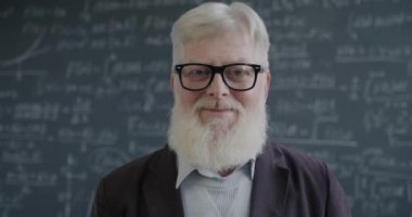 Takım elbiseli son sınıf öğrencisinin yavaş çekim portresi. Sınıfta durmuş kameraya bakıyor. Bilim ve eğitim kavramı.