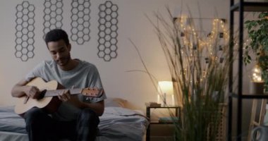 Akşamları yatak odasında gitar çalan yaratıcı Afrikalı Amerikalı bir adamın yavaş çekimi. Müzik ve gençlik kültürü kavramı.