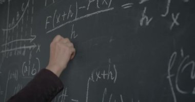 Erkek el yazısının matematik formülünü karatahtaya yazarken, profesör de sınıfta teoride çalışıyor. Eğitim ve bilim konsepti.