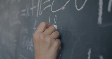 Kadın el öğretmeninin lisede fizik öğretmenliği yaparken karatahtaya semboller yazmasının yavaş çekimleri. Eğitim ve bilim konsepti.
