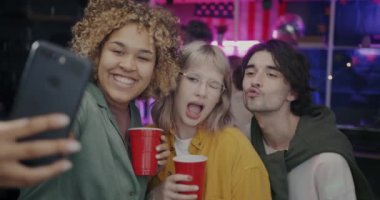 Akıllı telefon kamerasına poz veren kaygısız arkadaşlar gece partisinde içkilerle eğleniyorlar. Otoportre ve modern teknoloji konsepti.