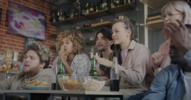 TV 'de spor maçı izleyen genç arkadaşların yavaş çekimleri evde üzgün ve hayal kırıklığına uğramış şekilde tezahürat yapmaları. Arkadaşlar ve duygu konsepti.
