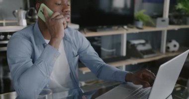 Afrikalı Amerikalı serbest çalışan cep telefonuyla konuşuyor ve evde çalışırken dizüstü bilgisayar kullanıyor. İş iletişimi ve serbest yazar kavramı.