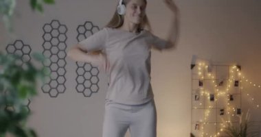 Yatakta dans eden, kulaklıkla müzik dinleyen, akşamları yatak odasında eğlenen mutlu genç bir kadın. Boş zaman aktivitesi ve gençlik yaşam tarzı konsepti.