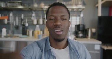 Mutlu Afro-Amerikalı bir adamın portresi çevrimiçi video görüşmesi yapıyor mutfaktaki kameraya bakarak konuşuyor. İletişim ve insan kavramı.