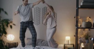 Yatakta dans eden neşeli erkek ve kadın müzik eşliğinde akşamları yatak odasında yaratıcı aktivitelerin tadını çıkarıyorlar. İlişki ve eğlence kavramı.