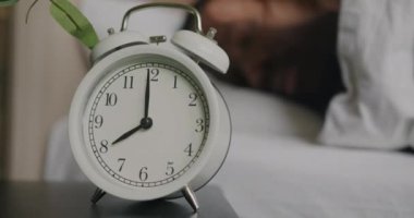 Erkek eli yavaş çekimde çalar saati kapatıyor. Rahat bir yatakta uyuyor ve dinleniyor. Ev kavramında boş zaman ve rahatlama.