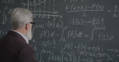 Formülün altını çizmeyi düşünen deneyimli üniversite profesörü sınıfta matematik çalışmasına odaklanmış durumda. Akademik eğitim ve halk konsepti.