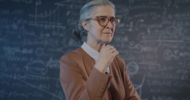 Düşünceli yaşlı bayanın yavaş hareket eden portresi. Sonra parmak kaldırıyor ve arka planda tahtaya karşı parlak bir fikir üretiyor. Araştırmacı ve beyin fırtınası konsepti.