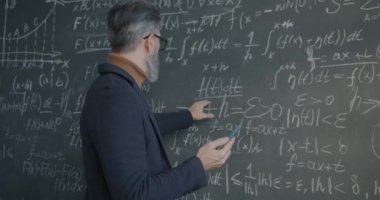 Modern profesör formülü karatahta üzerinde kontrol ediyor ve üniversite sınıfında bilime odaklı akıllı telefon uygulaması kullanıyor. Eğitim ve alet kavramı.