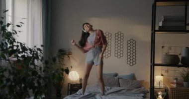 Genç Asyalı kadın pijama giyip yatakta dans ediyor müzik dinliyor ve sabahları yatak odasında boş vakit geçiriyor. Gençlik ve eğlence konsepti.