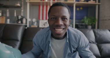 Heyecanlı Afro-Amerikan bir adamın evde kameraya bakarken spor tezahüratları izlediği yavaş çekim portresi. Hayran ve eğlence etkinliği konsepti.