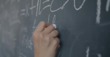Kadın el öğretmeninin lisede fizik öğretmenliği yaparken karatahtaya semboller yazmasının yavaş çekimleri. Eğitim ve bilim konsepti.