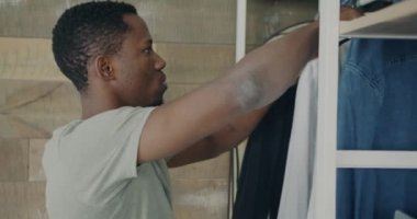 Çekici Afro-Amerikalı adam elbise askısı ve gardıropta şık kıyafetler seçiyor. Evde şık kıyafetler arıyor. İnsanlar ve tarz kavramı.