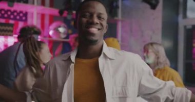 Neşeli Afrikalı Amerikalı adam kameraya bakıp dekore edilmiş dairede arkadaşlarıyla eğleniyor. Gençlik ve gece hayatı kavramı.