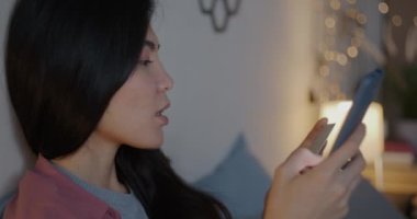 İnternetten alışveriş yapan neşeli Asyalı kadın. Akşamları yatakta otururken gülümseyen ve gülümseyen bir kredi kartıyla alışveriş yapıyor. Finans ve insanlar kavramı.