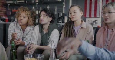 Spor hayranlarından oluşan çok ırklı bir grup kızlar ve erkekler TV 'de spor izliyorlar ve şişelerde içkiyle kadeh kaldırıyorlar apartmanda eğleniyorlar. Gençlik ve eğlence konsepti.