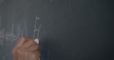 Sınıfta ders vermeye odaklanmış tebeşirle matematik formülü yazan kadın el öğretmeninin yakın çekimi. Bilgi ve bilim konsepti.