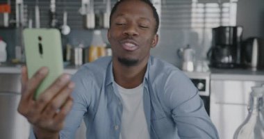 Neşeli Afro-Amerikalı adam çevrimiçi video görüşmesi yapıyor. Evdeki akıllı telefonuyla sanal görüşmenin keyfini çıkarıyor. İletişim ve insan kavramı.