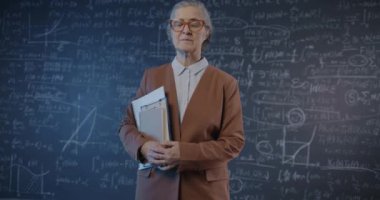 Yaşlı bir araştırmacının elinde kameraya bakan matematik sembolleriyle karatahta duvarına dayanmış yavaş çekimde portresi. Eğitim ve insanlar kavramı.