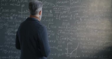 Erkek bilim adamının karatahtanın önünde durup matematik üzerine odaklanmış araştırma formülüne bakması yavaş bir hareket. Bilim ve eğitim kavramı.